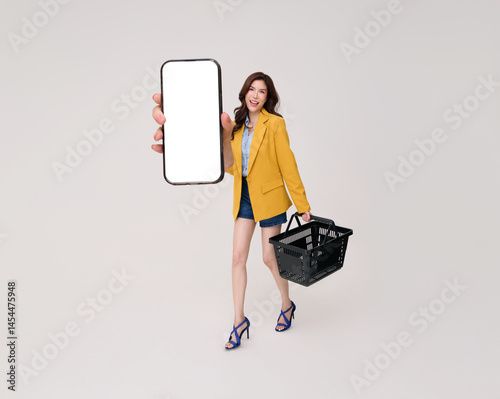 Happy Asian woman holding grocery shopping basket bag and showing smartphone mockup shopping grocery online isolated on white background.