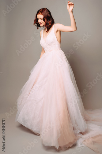 Adorable color-gradation wedding dress with deep sexy cut out. Funny studio full-length portrait of dancing ginger bride. Bridal outfit with lush tulle skirt. Seductive young woman in pink ball gown