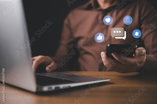A person in a brown shirt uses a smartphone and laptop simultaneously with floating social media icons, symbolizing digital communication, multitasking, and modern online connectivity.