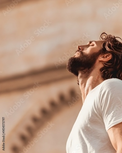 A man with a beard, head tilted back, breathes deeply in the sun's golden light against a blurred architectural backdrop