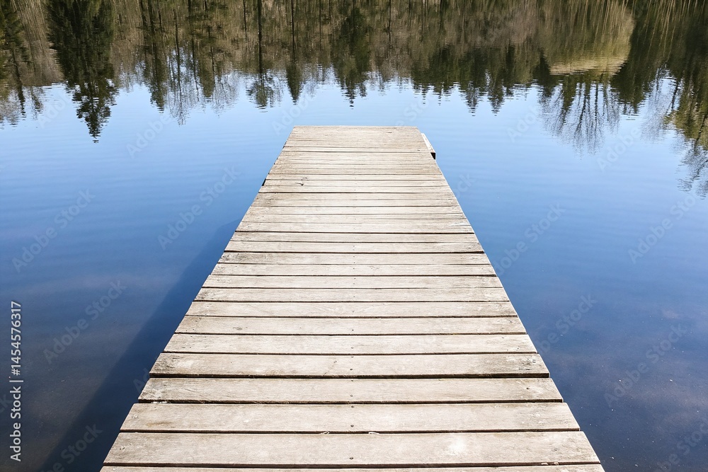Serene Wooden Dock Over Calm Lake Reflecting Lush Green Trees Under Clear Blue Sky Serene Wooden Dock Over Calm Lake Reflecting Lush Green Trees Under Clear Blue Sky