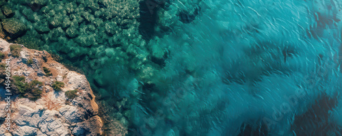 Aerial view of coastline with turquoise sea and deep blue ocean, summer. Rocky cliffs, greenery, waves, clear water. Scenic coastal seascape from drone.