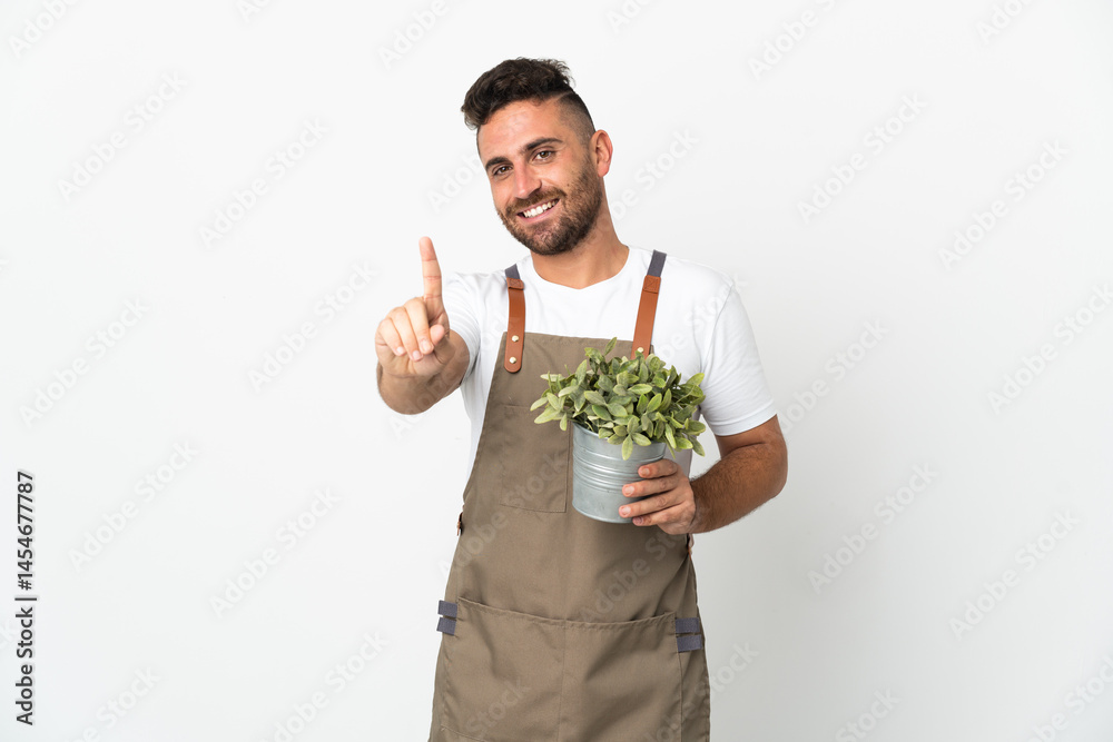 Gardener man holding a plant over isolated white background showing and lifting a finger Gardener man holding a plant over isolated white background showing and lifting a finger