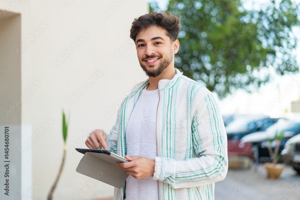 Fototapeta premium Handsome Arab man at outdoors touching the tablet screen with happy expression