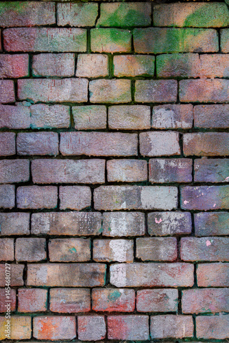 The brick wall is stained with multi-colored paints. The wall is covered with graffiti.