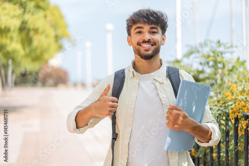 Young student Arabian man at outdoors with thumbs up because something good has happened