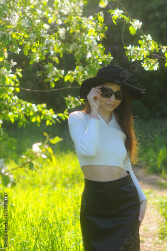 young girl walking in a summer park in a black hat in a white blouse and skirt