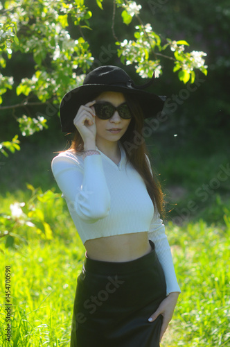 young girl walking in a summer park in a black hat in a white blouse and skirt