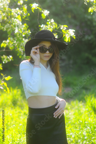young girl walking in a summer park in a black hat in a white blouse and skirt