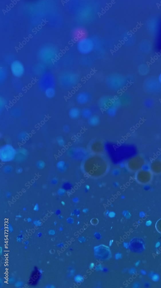 Vertical video. Sparkling oil. Glitter fluid flow. Defocused blue color shiny sequin particles liquid gloss texture paint water spill motion abstract art background with bokeh lights.