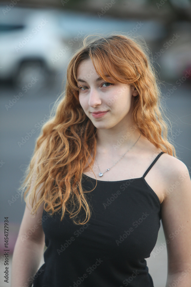 Fototapeta premium portrait of pretty teenage girl outdoors at dusk with city street and sky in background 