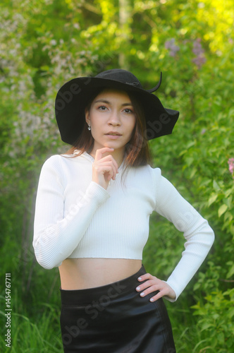 young girl walking in a summer park in a black hat in a white blouse and skirt