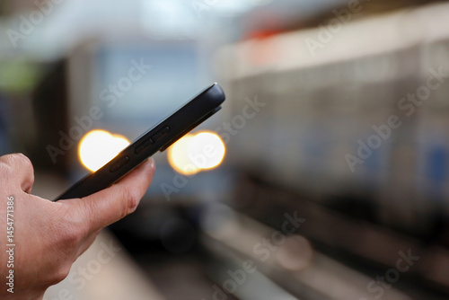Obraz na płótnie Smartphone in hand of woman waiting for the arriving train on railroad station. Commuter train passenger, online payment for the trip w salonie