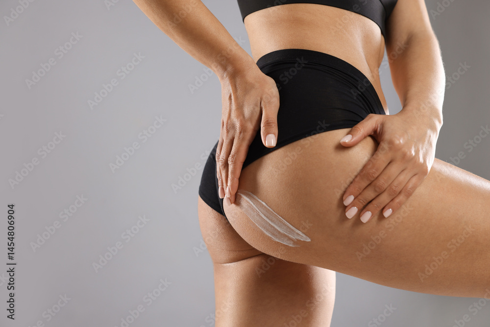 Fototapeta premium Woman applying anti cellulite cream on grey background, closeup. Space for text