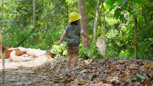 A Young Explorer Asian child dressed for adventure with Hat holding a net catching butterflies in a forest, ready to explore Discovering the wonders of nature in Lush Greenery