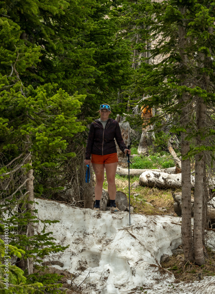 Woman Pauses on Snow Bank in Forest in Rocky Mountain Wilderness