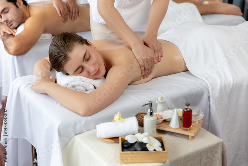 Caucasian couple customer enjoying relaxing anti-stress spa massage and pampering with beauty skin recreation leisure in day light ambient salon spa at luxury resort or hotel. Quiescent