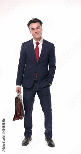 happy elegant man in navy blue suit holding bag, checking the time and nodding with his hand before walking away on white background