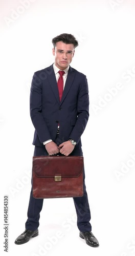 cool elegant businessman in navy blue suit with red tie holding suitcase while standing and being serious  in front of white background