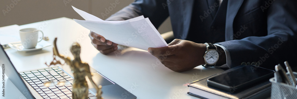 High angle view of unrecognizable Black male legal attorney working in office, looking through paper copy of document, header