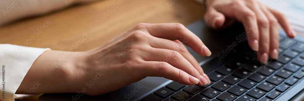 High angle closeup of hands of unrecognizable young woman typing on laptop while sitting at desk in office, header