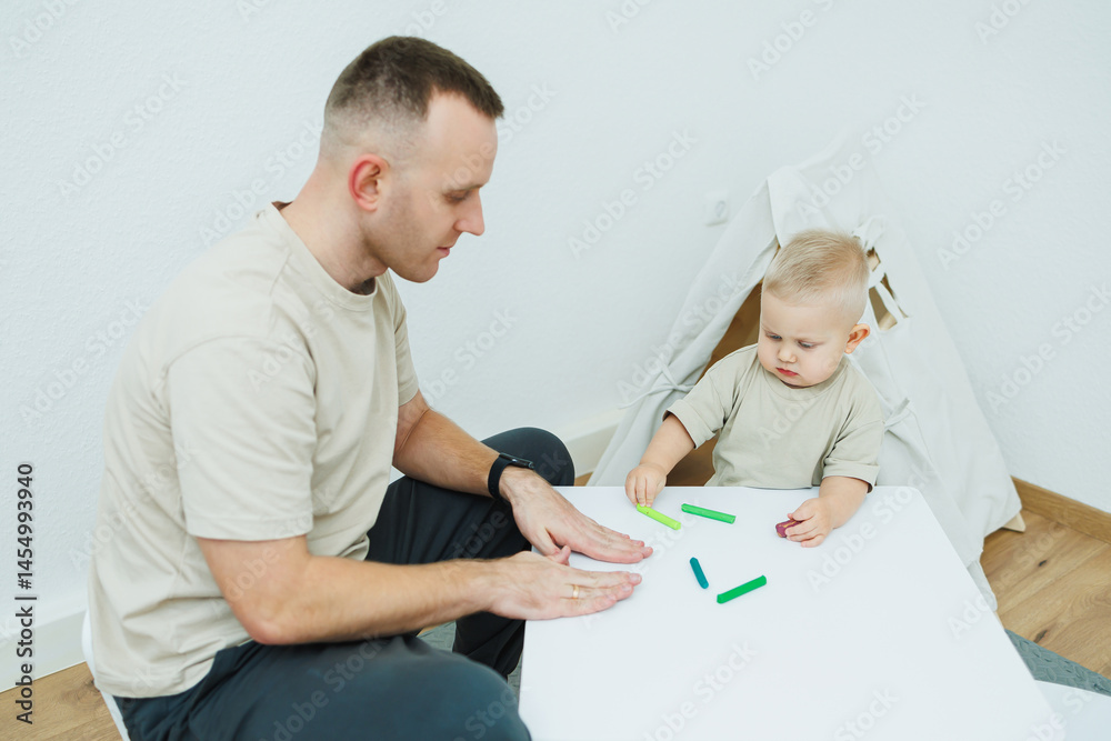 Dad teaches his 1.6 year old son to sculpt from plasticine. The toddler boy sits at the children's table with his dad and plays entertaining games. The child sculpts figures from plasticine