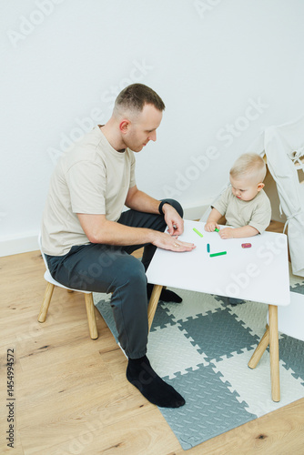 Obraz na płótnie Dad teaches his 1.6 year old son to sculpt from plasticine. The toddler boy sits at the children's table with his dad and plays entertaining games. The child sculpts figures from plasticine w salonie