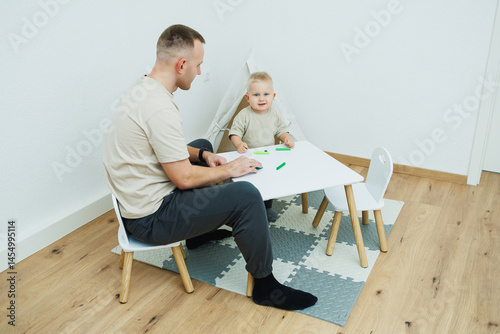 Obraz na płótnie Dad teaches his 1.6 year old son to sculpt from plasticine. The toddler boy sits at the children's table with his dad and plays entertaining games. The child sculpts figures from plasticine w salonie