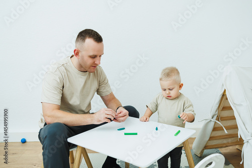 Obraz na płótnie Dad teaches his 1.6 year old son to sculpt from plasticine. The toddler boy sits at the children's table with his dad and plays entertaining games. The child sculpts figures from plasticine w salonie