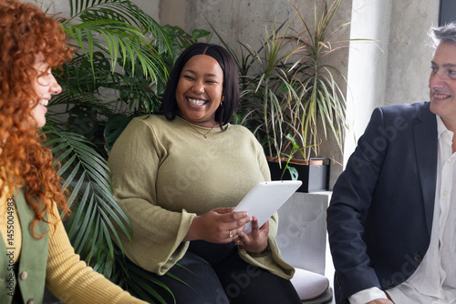Coworkers using tablet and smiling during business meeting in modern office