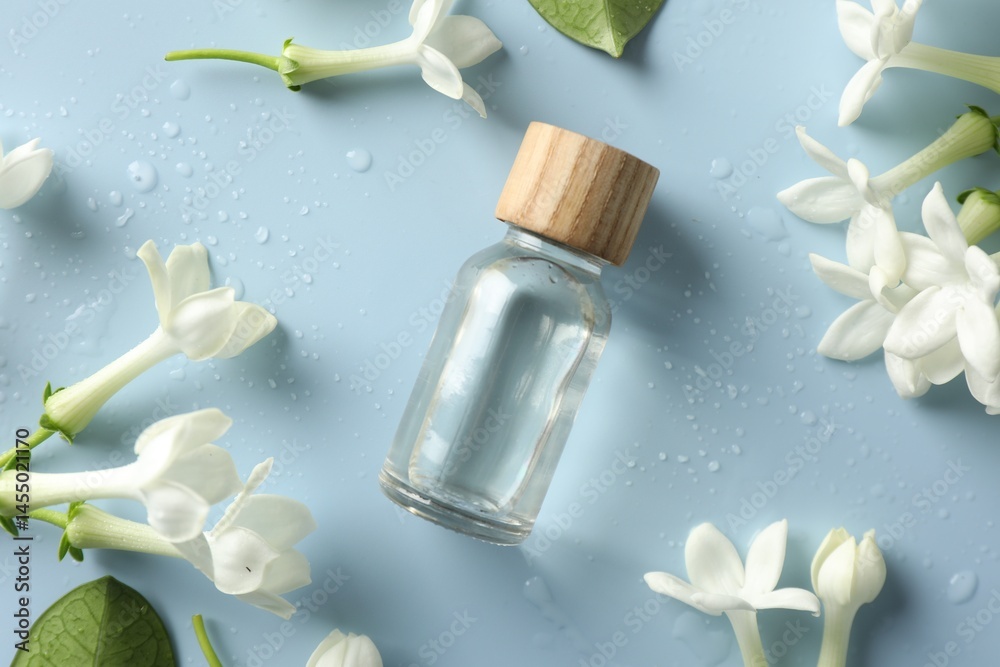 Bottle of essential oil and jasmine flowers on light blue background, flat lay Bottle of essential oil and jasmine flowers on light blue background, flat lay