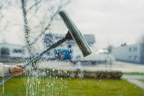 Obraz na płótnie Washing windows with glass cleaner and mop. Woman from a window cleaning company washes windows in the house. House cleaning with window washing. Mop for washing glass. w salonie