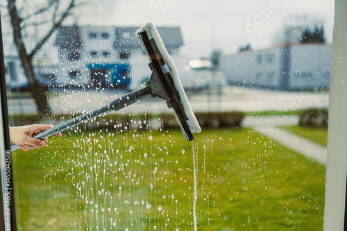Obraz na płótnie Washing windows with glass cleaner and mop. Woman from a window cleaning company washes windows in the house. House cleaning with window washing. Mop for washing glass. w salonie