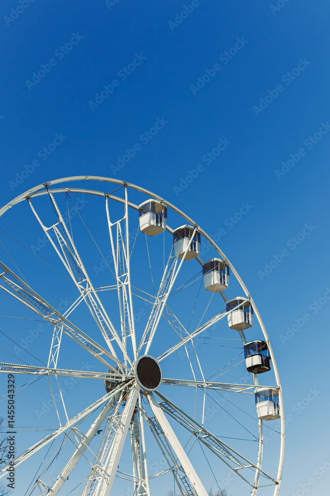 A large Ferris wheel against a blue sky. Cabins on the Ferris wheel.