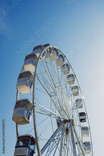 Obraz na płótnie A large Ferris wheel rises into the air with cabins against a blue sky. A Ferris wheel with enclosed cabins. w salonie