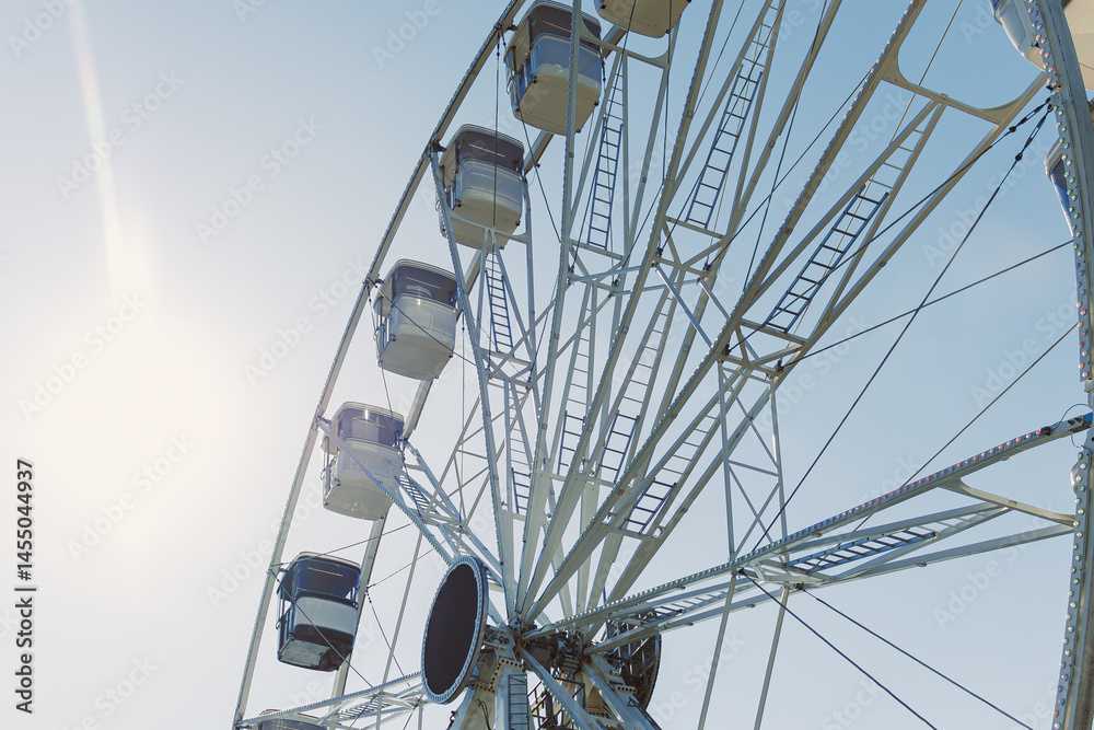 A large Ferris wheel rises into the air with cabins against a blue sky. A Ferris wheel with enclosed cabins.