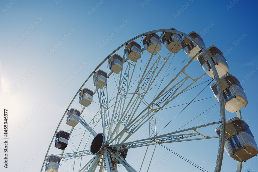 An attraction for viewing the city from above. A large Ferris wheel rises into the air with cabins against a blue sky. A Ferris wheel with closed cabins.