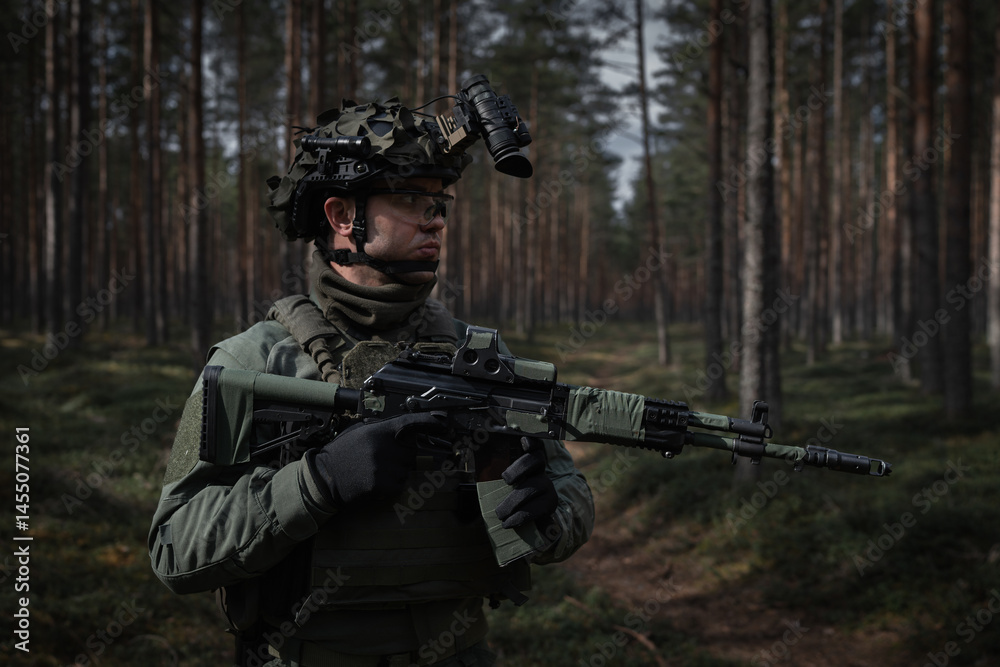 Fototapeta premium Fully equipped soldier in camouflage gear and helmet with night vision goggles holds an assault rifle during patrol in a dense forest.