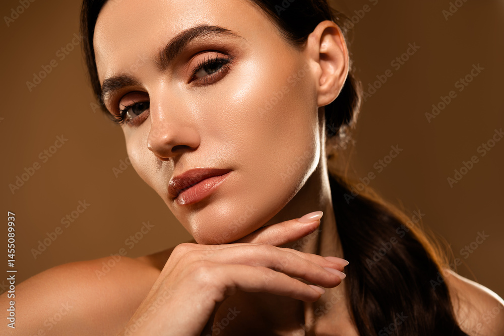 Fototapeta premium Portrait of a tempting young woman with glowing skin and natural makeup against a beige background