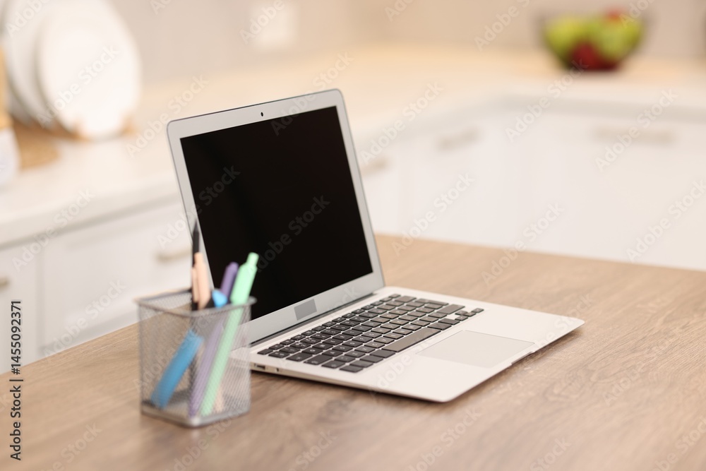 Laptop with blank screen and stationery on wooden table in kitchen, selective focus. Mockup for design Laptop with blank screen and stationery on wooden table in kitchen, selective focus. Mockup for design