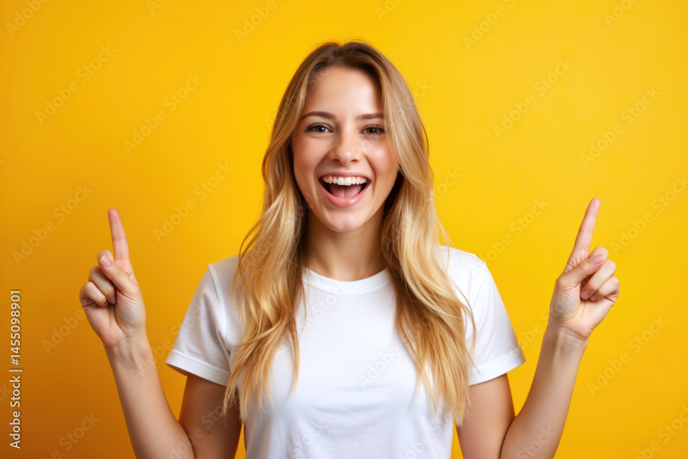 A cheerful woman with blonde hair, smiling broadly while pointing upwards with both hands against a bright yellow background.