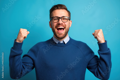 Obraz na płótnie A joyful man with glasses and a beard, wearing a sweater, celebrating with raised fists. w salonie