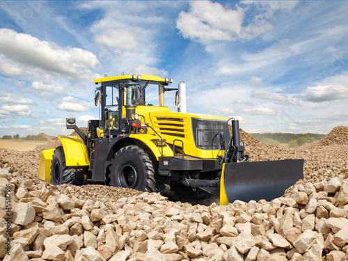 Bulldozer levels stones. Special construction equipment. Yellow bulldozer on territory of stone quarry. Front loader under blue sky. Construction bulldozer at time of preparation of construction site