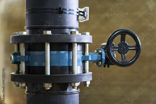Detailed Close-up of a Black Industrial Pipe with a Blue Flanged Valve and Handwheel for Manual Flow Control