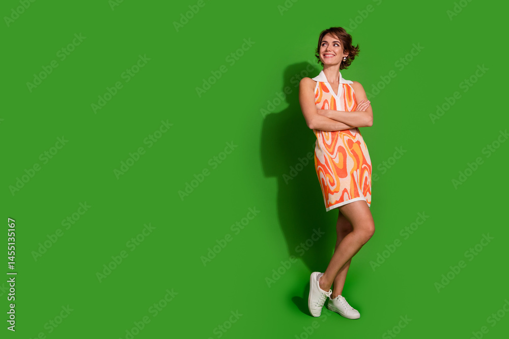 Full body photo of lovely young lady crossed hands look empty space dressed stylish colorful garment isolated on green color background