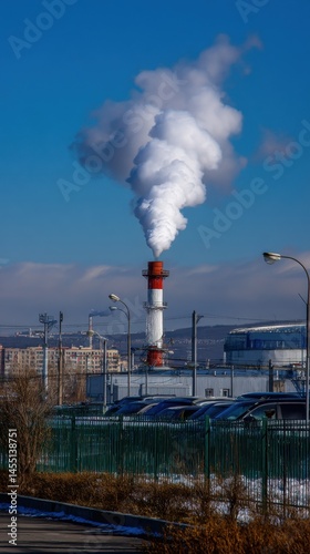 Industrial emissions with a tall smokestack releasing white smoke against a blue sky on a sunny day polluting the environment.