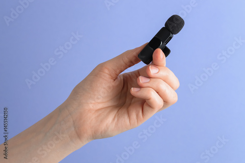 Woman holding lavalier microphone on light blue background, closeup