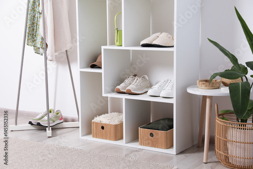Shelving unit with different footwear, accessories, clothes and houseplant indoors. Shoe storage