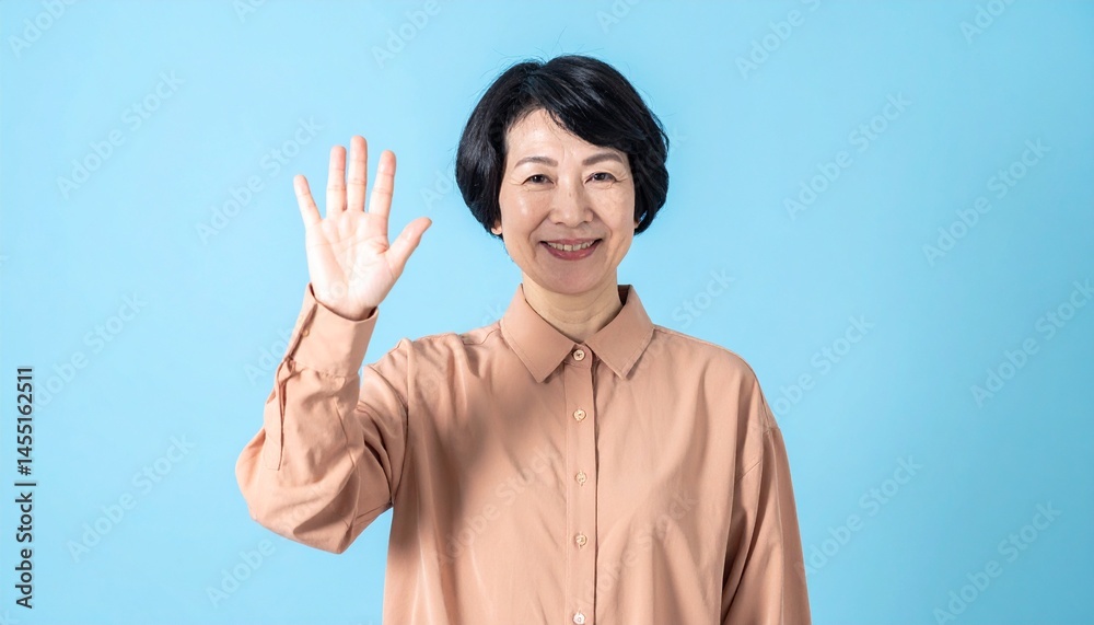 50代女性が「こんにちは」と話しかける姿、明るいブラウンのシャツとショートヘア、マットなスカイブルー背景が親しみやすく穏やかな印象

