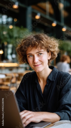 Smiling woman works with a laptop in a cafe setting, showcasing digital technology and a professional lifestyle.